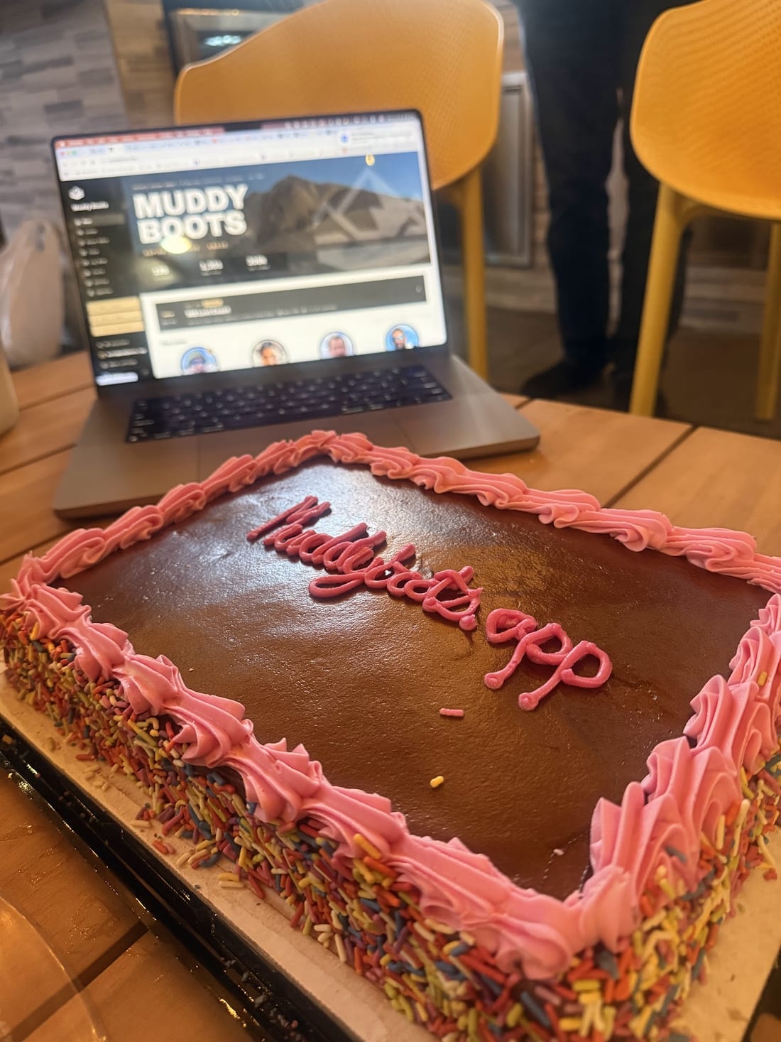 Launch-party cake reading muddyboots.app, with the app open on a laptop behind it